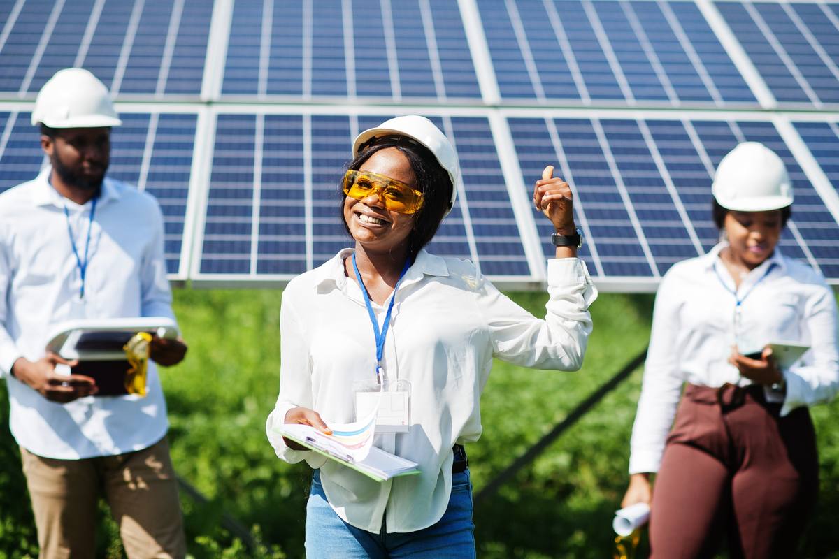 Smiling team in hard hats in front of a ground-mounted solar array